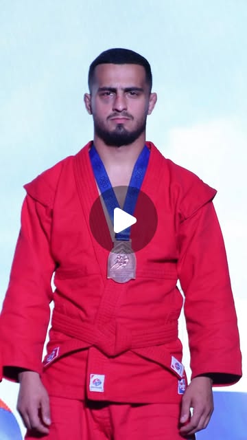 A fighter in a red SAMBO jacket wearing a bronze medal